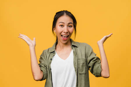 Young Asia lady feel happiness with positive expression, joyful surprise funky, dressed in casual cloth and looking at camera isolated on yellow background. Happy adorable glad woman rejoices success.の写真素材