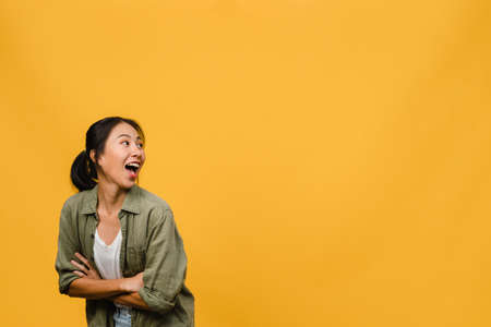 Portrait of young Asia lady with positive expression, arm crossed, smile broadly, dressed in casual cloth over yellow background. Happy adorable glad woman rejoices success. Facial expression concept.の写真素材