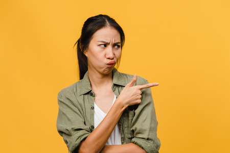 Young Asia Lady show something amazing at blank space with negative expression, excited screaming, crying emotional angry in casual clothing isolated over yellow background. Facial expression concept.の写真素材