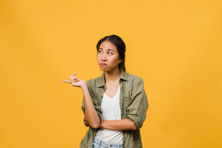 Young Asia Lady show something amazing at blank space with negative expression, excited screaming, crying emotional angry in casual clothing isolated over yellow background. Facial expression concept.の写真素材