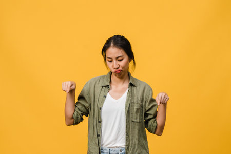 Young Asia Lady show something amazing at blank space with negative expression, excited screaming, crying emotional angry in casual clothing isolated over yellow background. Facial expression concept.の写真素材