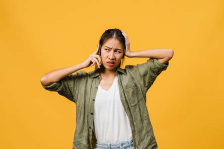 Young Asia lady talk by phone with negative expression, excited screaming, cry emotional angry in casual cloth and stand isolated on yellow background with blank copy space. Facial expression concept.の写真素材
