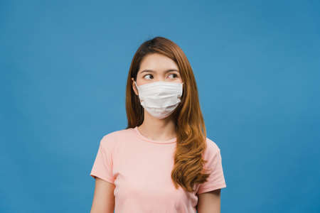 Young Asia girl wear medical face mask, tired of stress and tension, looks confidently at space isolated on blue background. Self-isolation, social distancing, quarantine for corona virus prevention.の写真素材