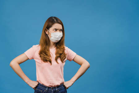 Young Asia girl wear medical face mask with negative expression, excited scream, crying emotional angry and look at camera isolated on blue background. Social distancing, quarantine for corona virus.の写真素材