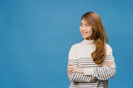 Portrait of young Asia lady with positive expression, arms crossed, smile broadly, dressed in casual clothing and looking at space over blue background. Happy adorable glad woman rejoices success.の写真素材