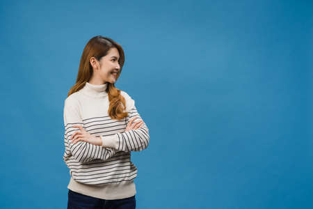 Portrait of young Asia lady with positive expression, arms crossed, smile broadly, dressed in casual clothing and looking at space over blue background. Happy adorable glad woman rejoices success.の写真素材