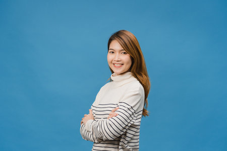 Portrait of young Asia lady with positive expression, arms crossed, smile broadly, dressed in casual clothing and looking at camera over blue background. Happy adorable glad woman rejoices success.の写真素材