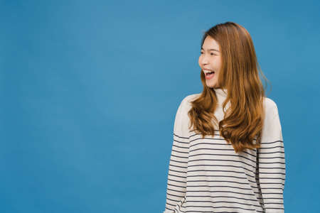 Portrait of young Asia lady with positive expression, smile broadly, dressed in casual clothing over blue background. Happy adorable glad woman rejoices success. Facial expression concept.の写真素材