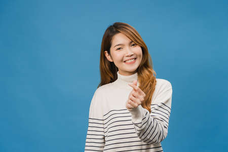 Young Asia lady with positive expression, shows hands gesture in heart shape, dressed in casual clothing and looking at camera isolated on blue background. Happy adorable glad woman rejoices success.の写真素材
