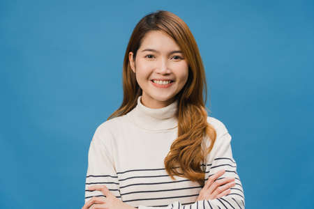 Portrait of young Asia lady with positive expression, arms crossed, smile broadly, dressed in casual clothing and looking at camera over blue background. Happy adorable glad woman rejoices success.の写真素材