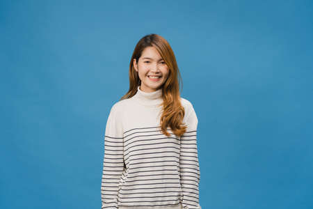 Young Asia lady with positive expression, smile broadly, dressed in casual clothing and looking at camera over blue background. Happy adorable glad woman rejoices success. Facial expression concept.の写真素材