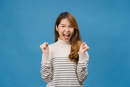 Young Asia lady feeling happiness with positive expression, joyful surprise funky, dressed in casual cloth and looking at camera isolated on blue background. Happy adorable glad woman rejoices successの写真素材