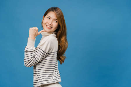 Portrait of young Asian lady smiling with cheerful expression, shows something amazing at blank space in casual clothing and standing isolated over blue background. Facial expression concept.の写真素材