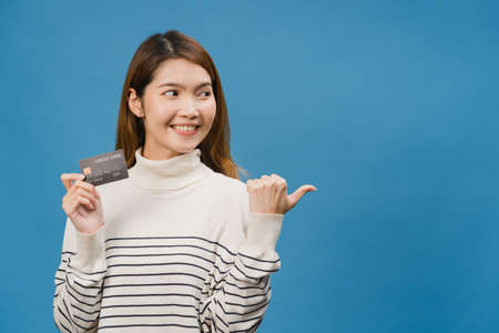 Young Asia lady show credit bank card with positive expression, smiles broadly, dressed in casual clothing feeling happiness and stand isolated on blue background. Facial expression concept.の写真素材