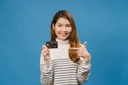 Young Asia lady show credit bank card with positive expression, smiles broadly, dressed in casual clothing feeling happiness and stand isolated on blue background. Facial expression concept.の写真素材