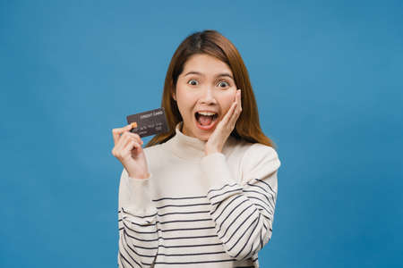 Young Asia lady show credit bank card with positive expression, smiles broadly, dressed in casual clothing feeling happiness and stand isolated on blue background. Facial expression concept.の写真素材
