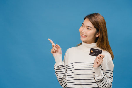Young Asia lady show credit bank card with positive expression, smiles broadly, dressed in casual clothing feeling happiness and stand isolated on blue background. Facial expression concept.の写真素材
