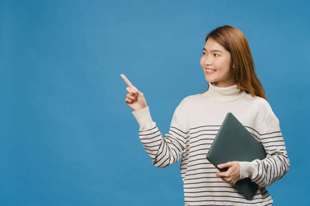 Young Asia lady using laptop with positive expression, smiles broadly, dressed in casual clothing feeling happiness and stand isolated on blue background. Happy adorable glad woman rejoices success.の写真素材