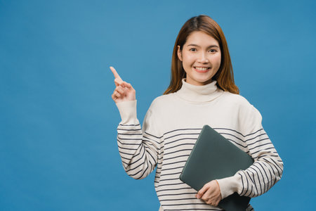 Young Asia lady using laptop with positive expression, smiles broadly, dressed in casual clothing feeling happiness and stand isolated on blue background. Happy adorable glad woman rejoices success.の写真素材