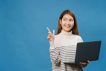 Young Asia lady using laptop with positive expression, smiles broadly, dressed in casual clothing feeling happiness and stand isolated on blue background. Happy adorable glad woman rejoices success.の写真素材