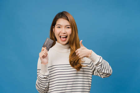 Young Asia lady show credit bank card with positive expression, smiles broadly, dressed in casual clothing feeling happiness and stand isolated on blue background. Facial expression concept.の写真素材