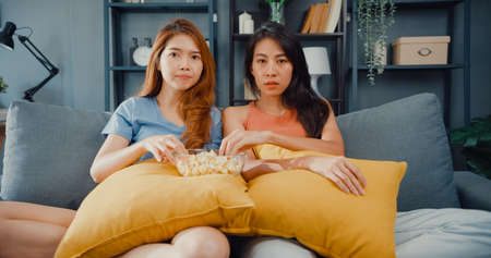Asia housewife women with casual relax on couch with cup of tea talk together about their life and husband relationship gossip in living room at house. Girls friends roommate stay in dorm together.の写真素材
