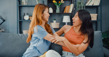 Asia housewife women with casual relax on couch with cup of tea talk together about their life and husband relationship gossip in living room at house. Girls friends roommate stay in dorm together.の写真素材