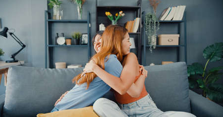 Asia housewife women with casual relax on couch with cup of tea talk together about their life and husband relationship gossip in living room at house. Girls friends roommate stay in dorm together.の写真素材