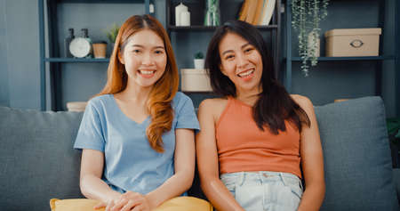 Asia housewife women with casual relax on couch with cup of tea talk together about their life and husband relationship gossip in living room at house. Girls friends roommate stay in dorm together.の写真素材