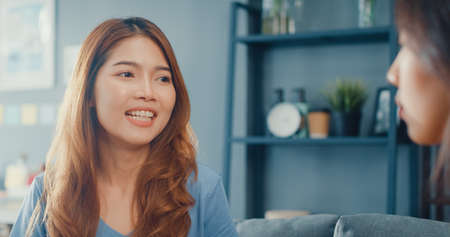 Asia housewife women with casual relax on couch with cup of tea talk together about their life and husband relationship gossip in living room at house. Girls friends roommate stay in dorm together.の写真素材