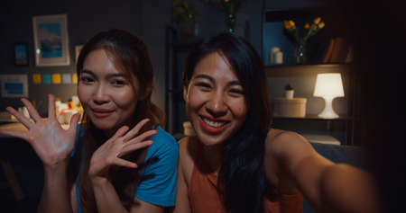 Happy attractive Asia women with casual relax on couch chat talk together about their life and relationship gossip in living room at house night. Girls friends roommate stay in dorm together.の写真素材