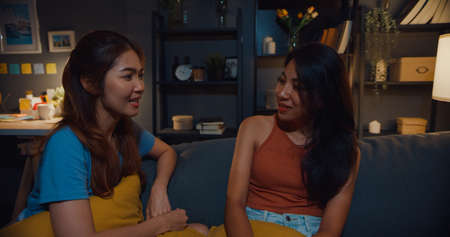 Happy attractive Asia women with casual relax on couch chat talk together about their life and relationship gossip in living room at house night. Girls friends roommate stay in dorm together.の写真素材