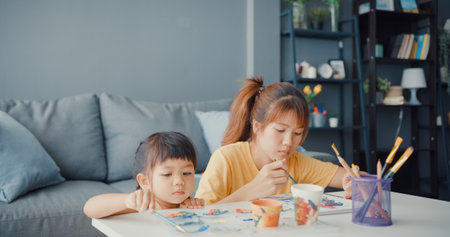 Happy cheerful Asia family mom teach toddler girl paint ceramic pot having fun relax on table in living room at house. Spending time together, Social distance, Quarantine for coronavirus prevention.の写真素材