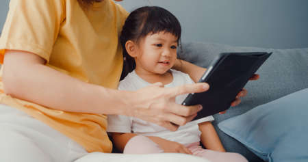 Happy cheerful Asia family mom teach toddler girl paint ceramic pot having fun relax on table in living room at house. Spending time together, Social distance, Quarantine for coronavirus prevention.の写真素材
