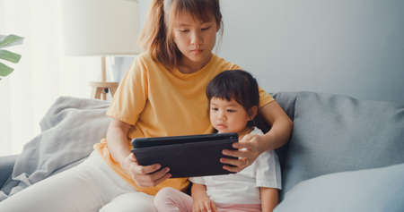 Happy cheerful Asia family mom teach toddler girl paint ceramic pot having fun relax on table in living room at house. Spending time together, Social distance, Quarantine for coronavirus prevention.の写真素材