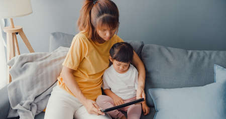 Happy cheerful Asia family mom teach toddler girl paint ceramic pot having fun relax on table in living room at house. Spending time together, Social distance, Quarantine for coronavirus prevention.の写真素材
