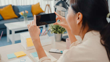 Young Asia lady use smart phone with blank black screen mock up display for advertising text while smart working from home at living room. Chroma key technology, Marketing design concept.の写真素材