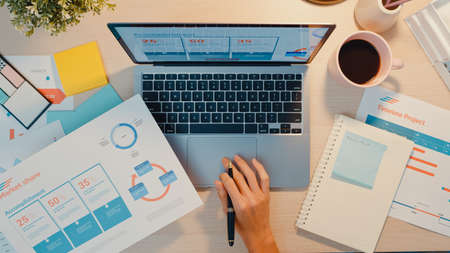 Top view of young Asia business lady freelance focus on laptop write worksheet finance graph account chart market plan at office night. Work from home, remotely, distance education coronavirus conceptの写真素材