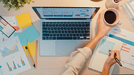 Asia businesswoman using laptop with blank white screen mock up display for advertising text talk to colleagues about plan in video call meeting at living room at house. Working overload at night.の写真素材