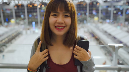 Happy Asian woman smiling to camera while staying at terminal in international airport, female tourist ready to travel on vacation. Lifestyle women happy holiday in the airport concept.の写真素材
