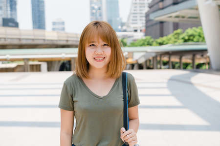 Attractive casual happy young Asian woman in international airport, using and checking her smartphone standing in terminal hall while waiting for her flight to board airplane at the departure gate.の写真素材