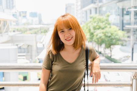 Attractive casual happy young Asian woman in international airport, using and checking her smartphone standing in terminal hall while waiting for her flight to board airplane at the departure gate.の写真素材