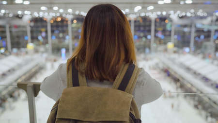 Attractive casual happy young Asian woman in international airport, using and checking her smartphone standing in terminal hall while waiting for her flight to board airplane at the departure gate.の写真素材