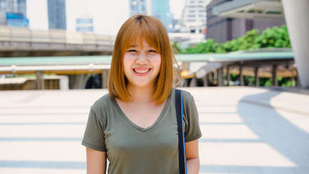 Attractive casual happy young Asian woman in international airport, using and checking her smartphone standing in terminal hall while waiting for her flight to board airplane at the departure gate.の写真素材