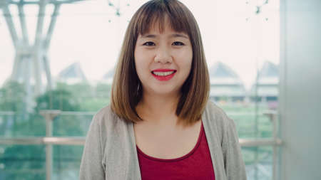Attractive casual happy young Asian woman in international airport, using and checking her smartphone standing in terminal hall while waiting for her flight to board airplane at the departure gate.の写真素材