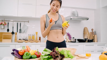 Young Asian woman drinking orange juice in the kitchen, beautiful female in sport clothing use organic fruits lots of nutrition making orange juice by herself at home. Healthy food concept.の写真素材
