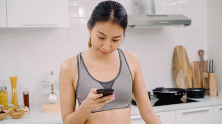 Young Asian woman drinking orange juice in the kitchen, beautiful female in sport clothing use organic fruits lots of nutrition making orange juice by herself at home. Healthy food concept.の写真素材