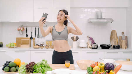 Happy Asian woman using tablet for looking recipe while making food in the kitchen, female use organic vegetable for healthy food at home. Lifestyle women making food concept.の写真素材