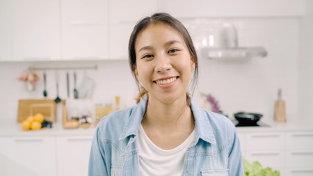 Happy Asian woman using tablet for looking recipe while making food in the kitchen, female use organic vegetable for healthy food at home. Lifestyle women making food concept.の写真素材