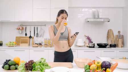 Happy Asian woman using tablet for looking recipe while making food in the kitchen, female use organic vegetable for healthy food at home. Lifestyle women making food concept.の写真素材